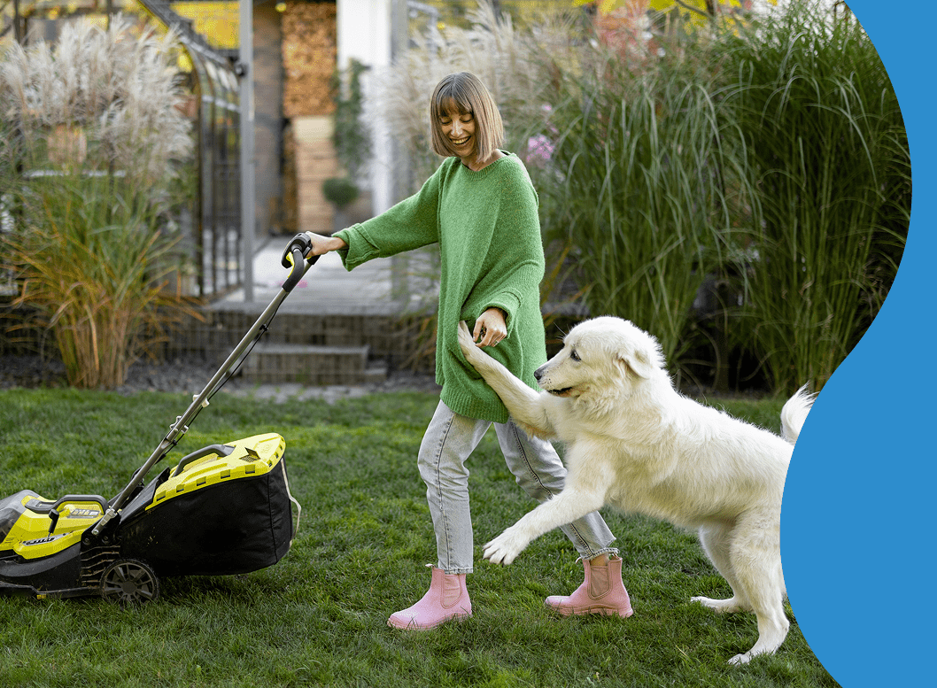 Woman mowing lawn with playful dog.